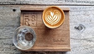 Ristr8to latte art and a glass of water served on a branded wooden R8 tray