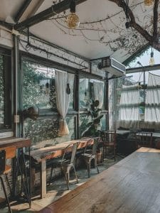 The Barn Eatery and Design's greenhouse interior with wooden tables and greenery-filled windows
