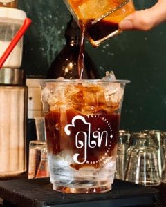Iced house-roasted coffee poured into a branded cup at The Brewing House by Rue Thai