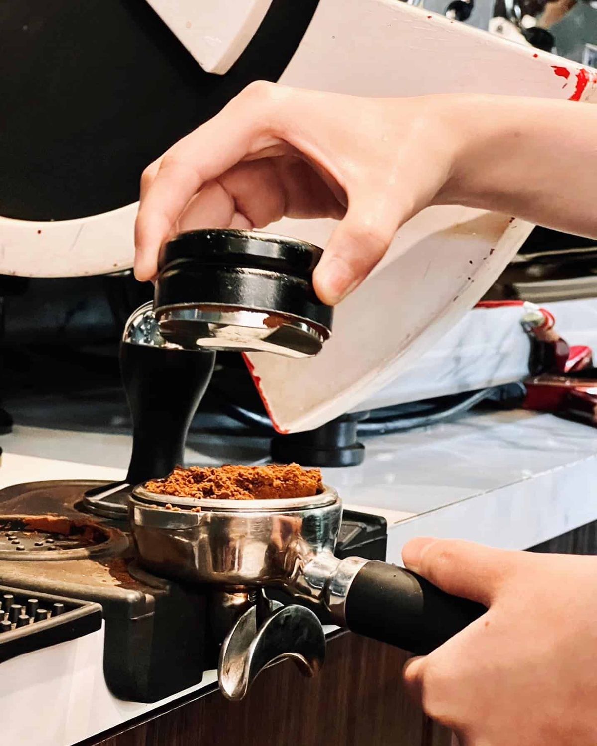 Barista tamping freshly ground coffee into a portafilter at The Brewing House by Rue Thai