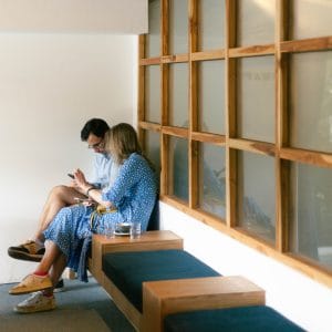 Two customers on GRAPH quarter's wooden bench beside a grid of timber-framed windows