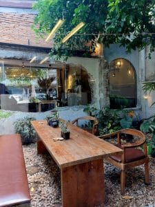 Fringe.th's leafy courtyard with a long wooden table, rattan chair and arched mirror