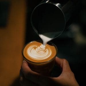 Barista pouring a rosetta of latte art into an espresso drink at GRAPH quarter