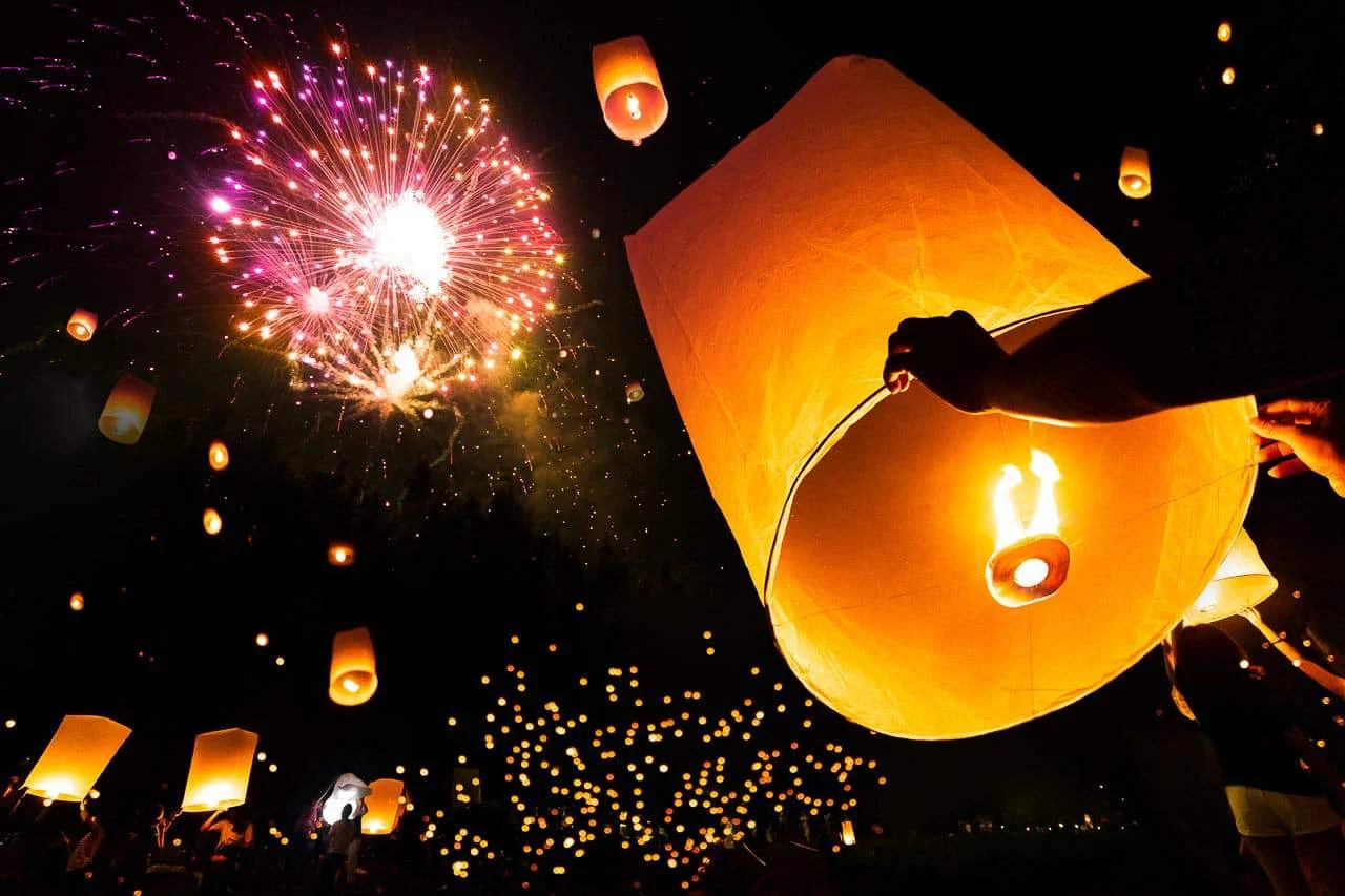 Hands releasing a glowing sky lantern at a Yi Peng celebration