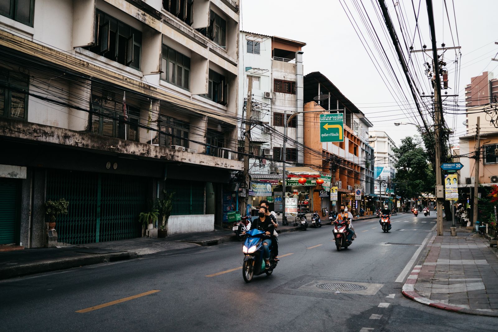 Motorbikes riding down a Chiang Mai street lined with shophouses and tangled power lines