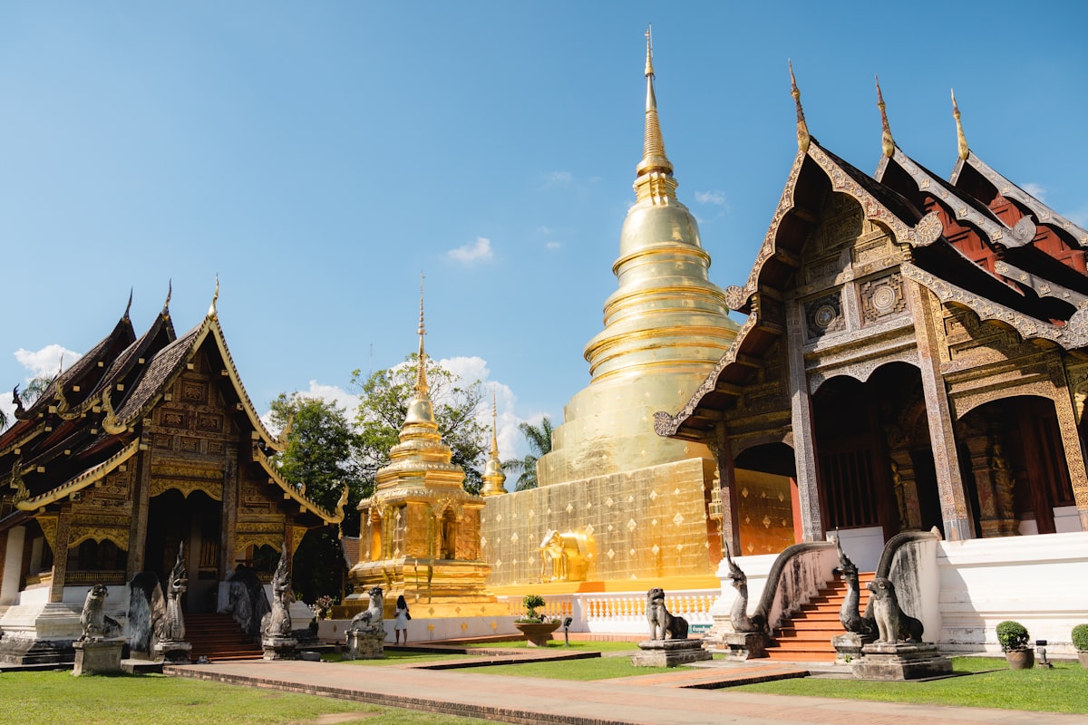 Golden chedi and ornate Lanna temple buildings under a blue sky in Chiang Mai